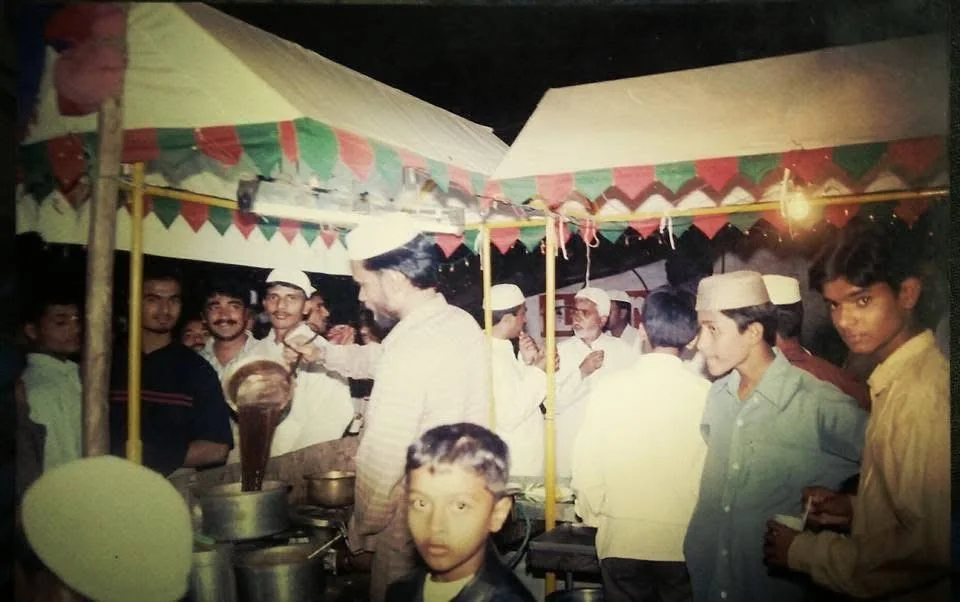 A man in a white cap pouring tea from a large pot into a cup at the stall while customers look on